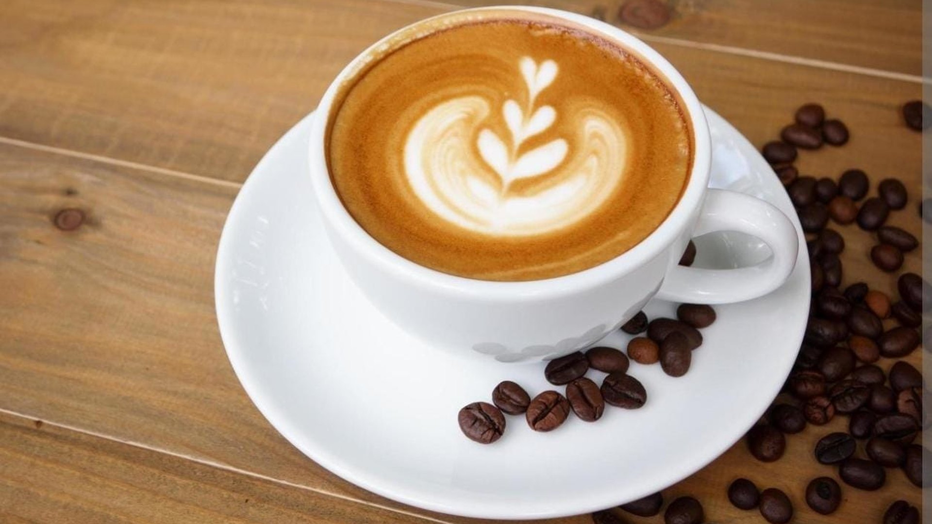 Precision latte art cappuccino with whole roasted coffee beans on polished wood